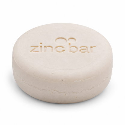 DermaHarmony Zinc Shampoo Bar 2% Pyrithione Zinc Tea Tree 113 g - A round beige zinc soap bar with embossed text