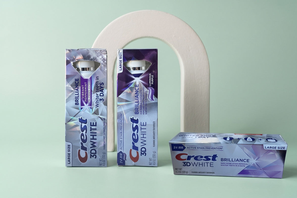 Crest 3D White Brilliance toothpaste cartons standing and lying on a pale mint studio backdrop